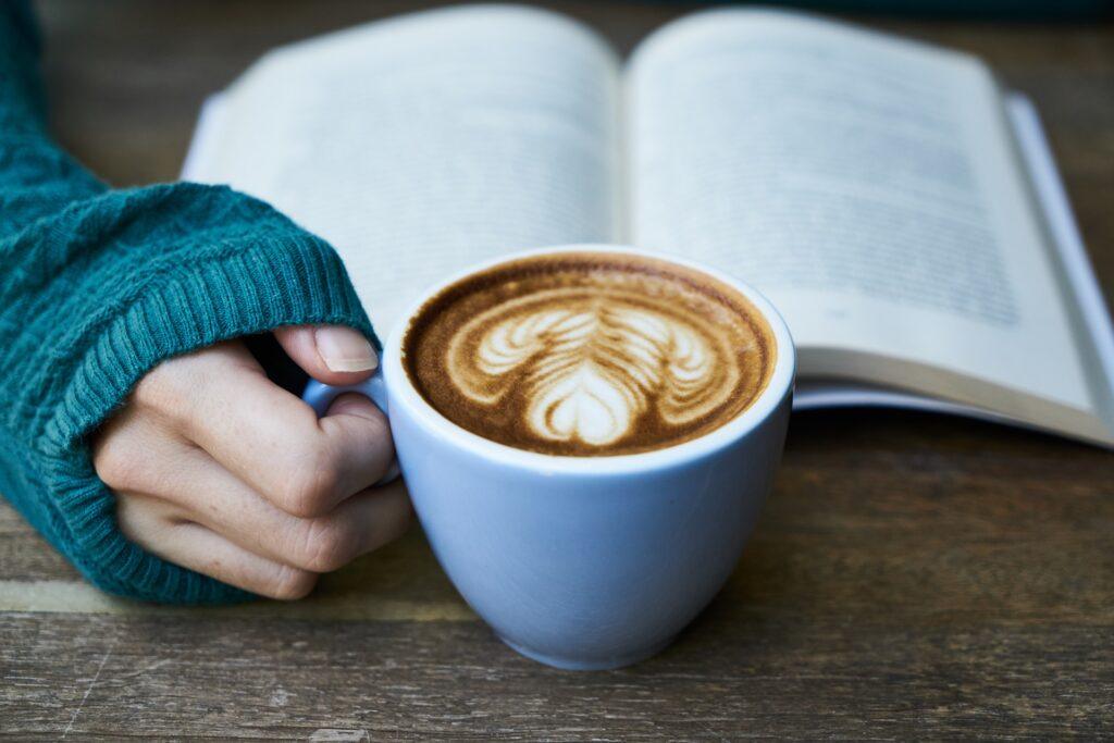 Hand holding a coffee mug in front of a book.