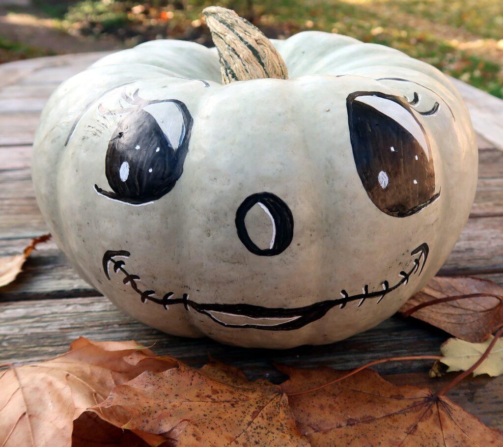 White pumpkin with painted eyes, nose, and mouth.