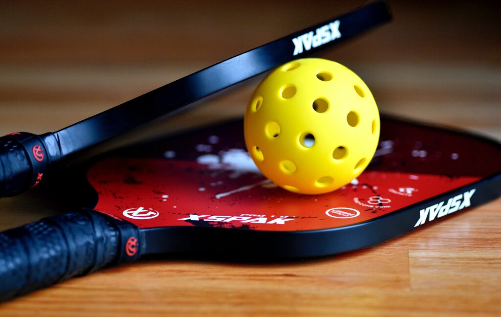 Yellow pickleball resting on two red paddles with black handles.