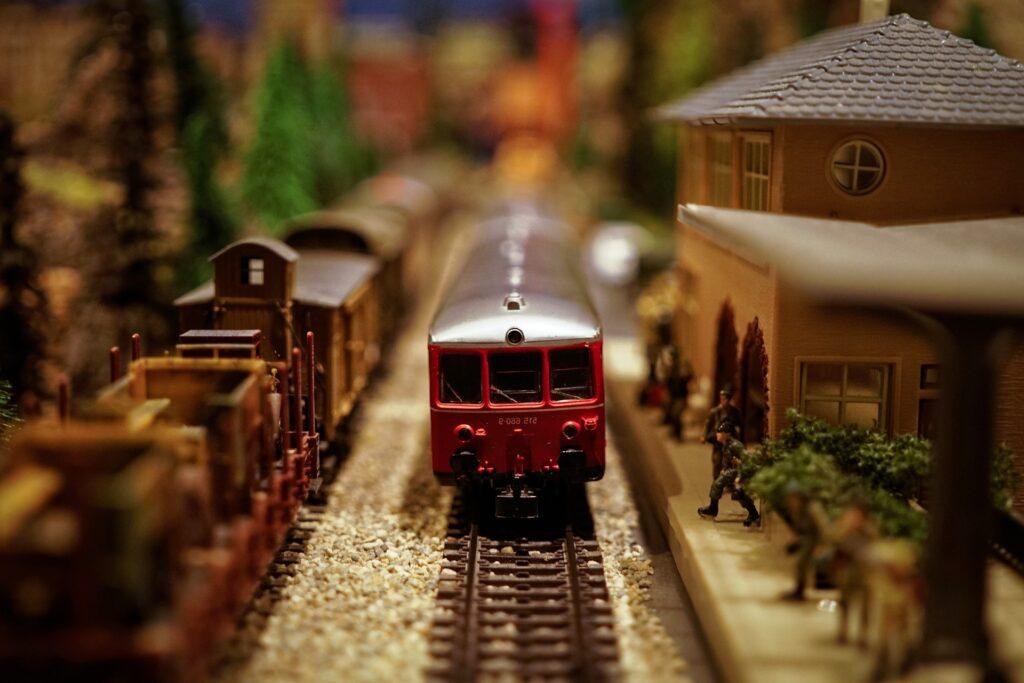 Red model train on tracks, surrounded by miniature buildings and figurines, creating a lively scene.