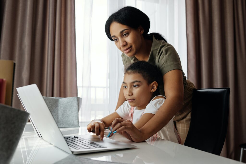 Adult assisting child with laptop at a table.