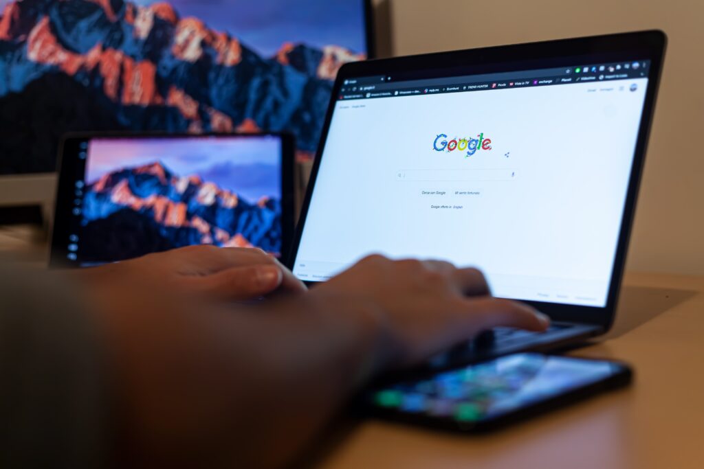 Hands typing on a laptop with Google open, surrounded by screens displaying mountain scenery.