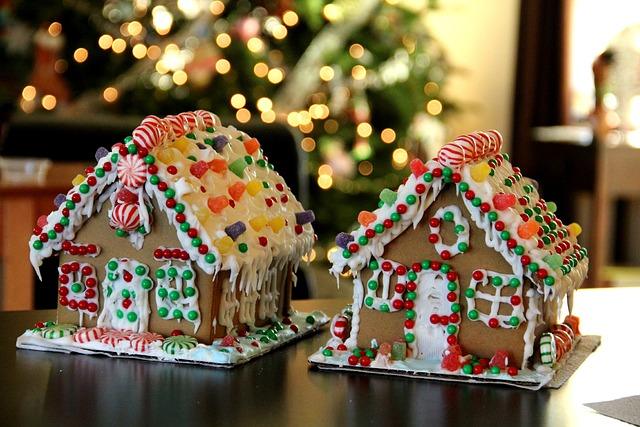 Two colorful gingerbread houses decorated with candy sit on a table, with a Christmas tree in the background.