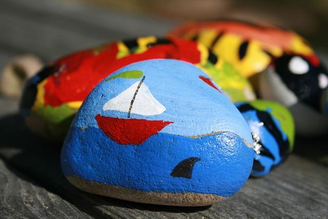 Colorful rock art with a sailboat and shark fin on a blue background, displayed outdoors.
