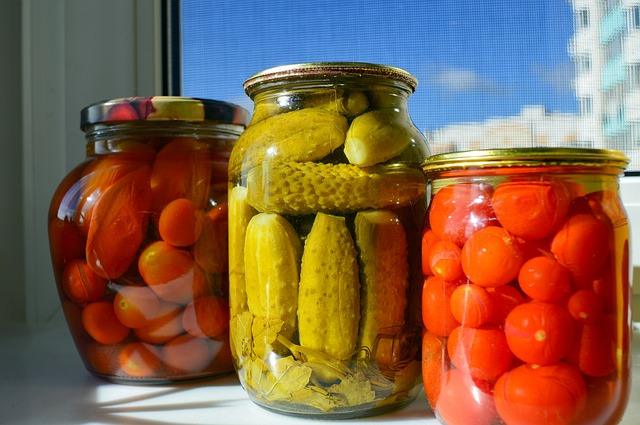 Jars of pickled cucumbers and tomatoes on a sunny windowsill.