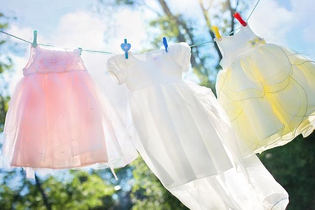 Three pastel dresses hang on a clothesline against a sunny, blue sky background.