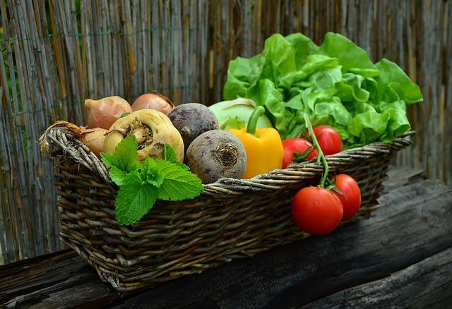 Basket of fresh vegetables including lettuce, tomatoes, and peppers on a rustic wooden surface.